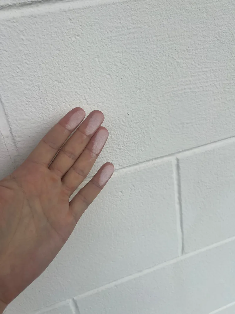 White chalky paint residue visible on fingertips after touching a painted surface
